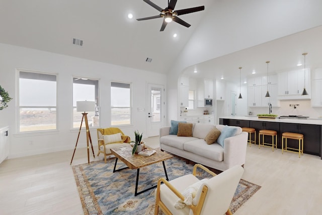 living room with plenty of natural light, high vaulted ceiling, ceiling fan, and light wood-type flooring