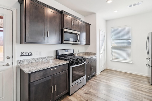 kitchen featuring dark brown cabinetry, light hardwood / wood-style flooring, light stone countertops, and appliances with stainless steel finishes