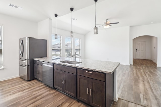 kitchen featuring sink, light stone counters, hanging light fixtures, stainless steel appliances, and light hardwood / wood-style floors