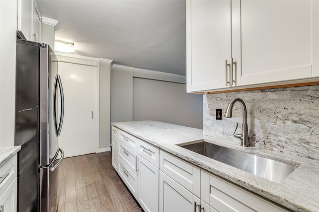 kitchen featuring stainless steel fridge, light stone countertops, sink, and white cabinets