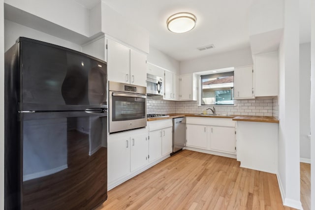 kitchen featuring appliances with stainless steel finishes, light wood-type flooring, decorative backsplash, and white cabinets