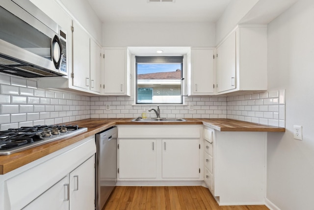 kitchen with appliances with stainless steel finishes, butcher block countertops, sink, and white cabinets