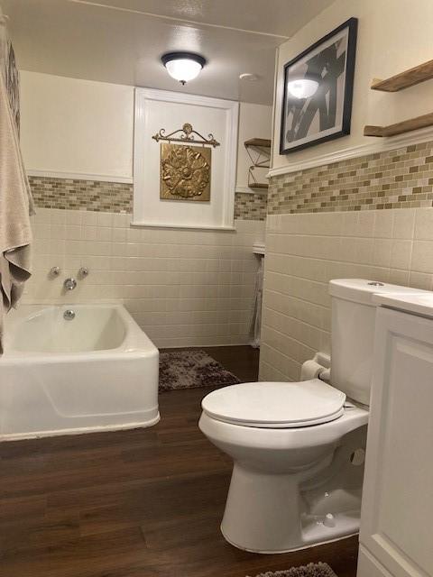 bathroom with tile walls, hardwood / wood-style flooring, toilet, and a bathing tub