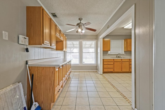 kitchen with sink, crown molding, light tile patterned floors, ceiling fan, and a textured ceiling