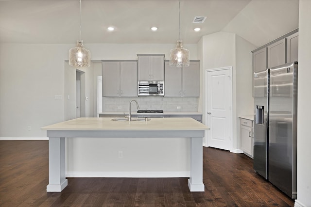 kitchen featuring decorative light fixtures, sink, gray cabinetry, stainless steel appliances, and a center island with sink