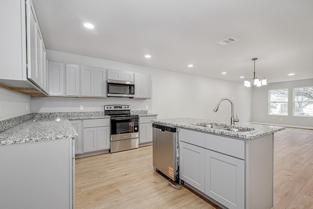 kitchen with sink, decorative light fixtures, light hardwood / wood-style flooring, an island with sink, and stainless steel appliances