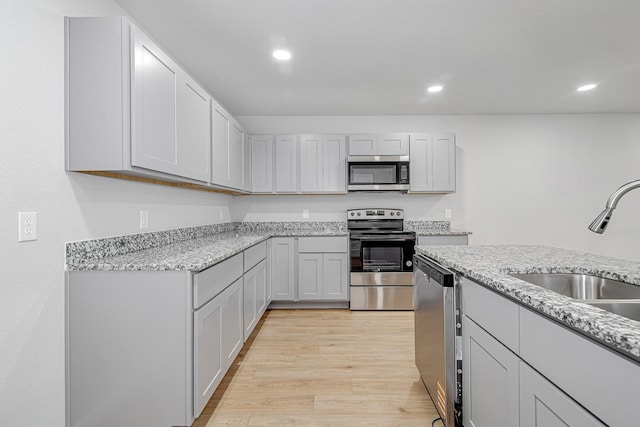 kitchen featuring stainless steel appliances, light hardwood / wood-style floors, sink, and light stone countertops