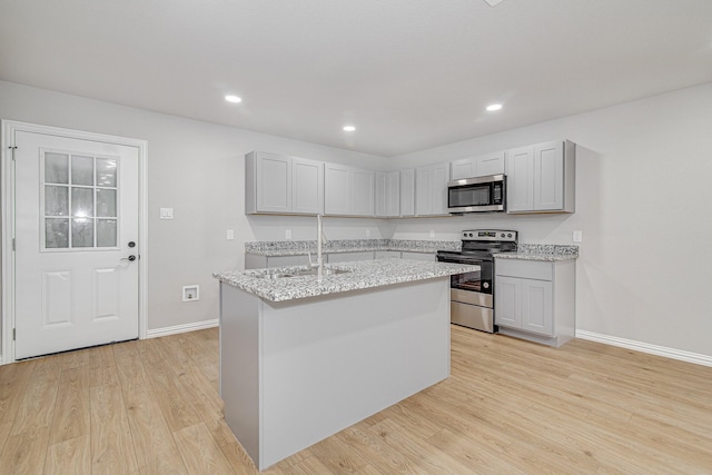 kitchen with sink, a kitchen island with sink, light stone counters, stainless steel appliances, and light wood-type flooring