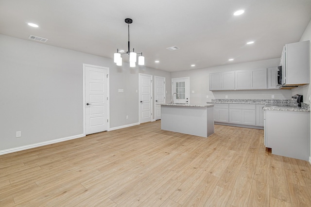 kitchen with range, decorative light fixtures, a center island with sink, light hardwood / wood-style flooring, and white cabinets