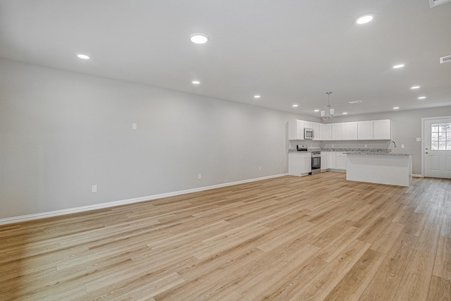 unfurnished living room featuring an inviting chandelier and light hardwood / wood-style floors