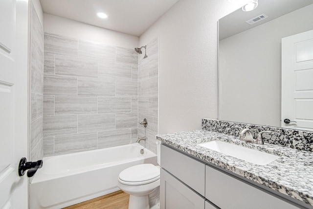 full bathroom with tiled shower / bath combo, vanity, hardwood / wood-style flooring, and toilet