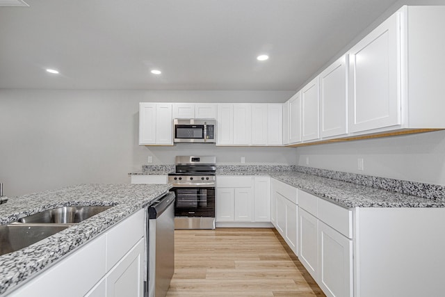 kitchen with sink, white cabinetry, stainless steel appliances, light stone counters, and light hardwood / wood-style floors