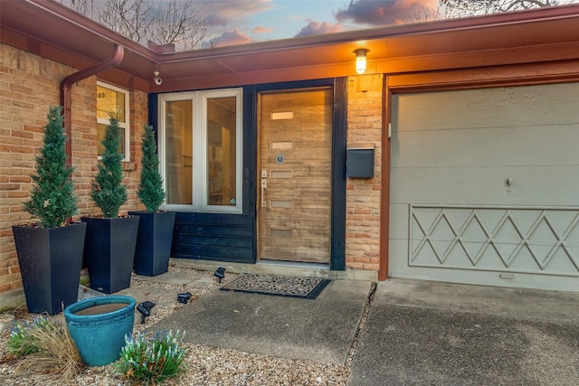 entrance to property with a garage, concrete driveway, and brick siding