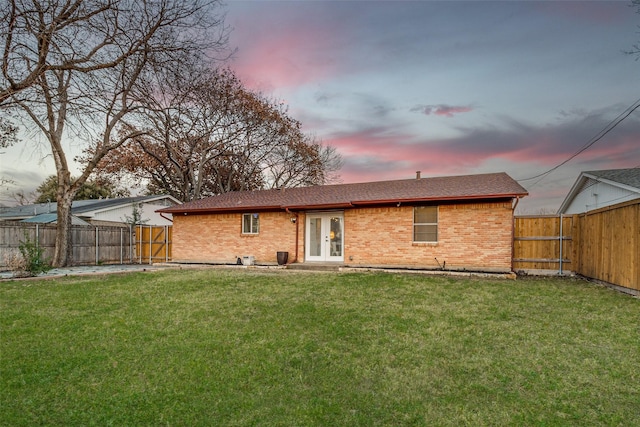 back house at dusk featuring french doors and a lawn