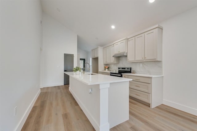 kitchen featuring electric stove, sink, lofted ceiling, a kitchen island with sink, and backsplash