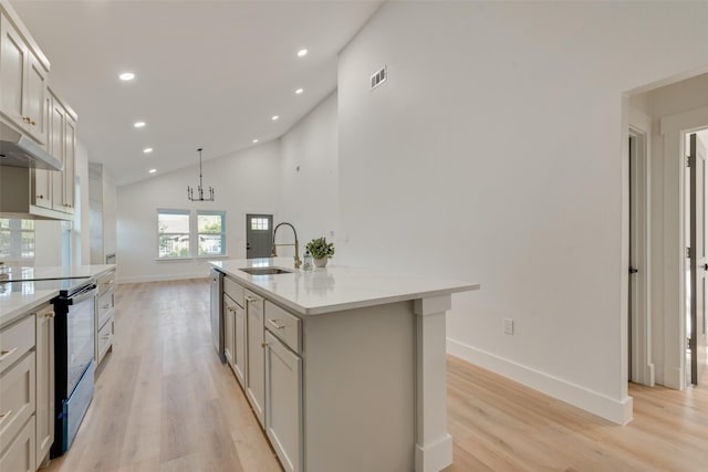 kitchen with sink, light hardwood / wood-style flooring, black range with electric stovetop, a center island with sink, and decorative light fixtures