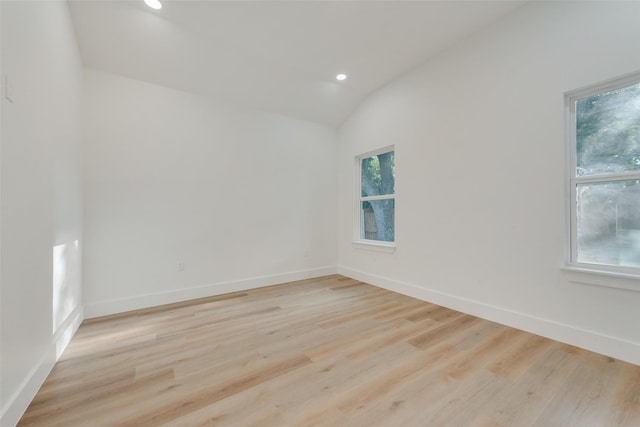 empty room featuring plenty of natural light, lofted ceiling, and light hardwood / wood-style flooring