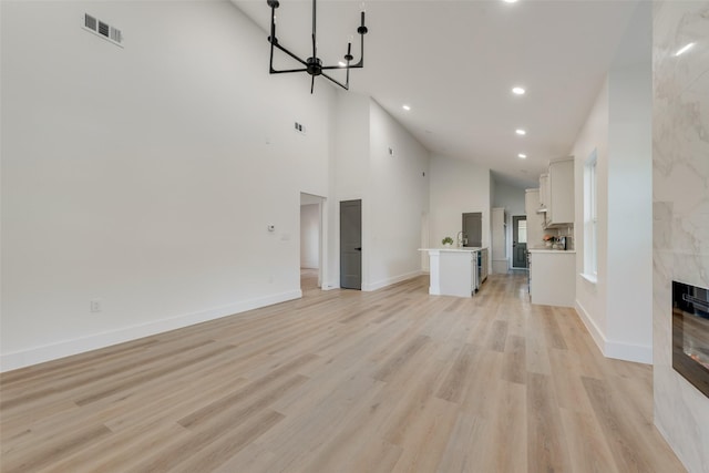 unfurnished living room featuring a premium fireplace, high vaulted ceiling, and light hardwood / wood-style flooring