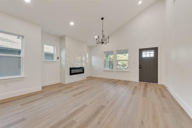 unfurnished living room featuring heating unit, high vaulted ceiling, a fireplace, a chandelier, and light hardwood / wood-style floors