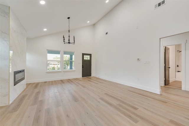 unfurnished living room with heating unit, high vaulted ceiling, a high end fireplace, an inviting chandelier, and light hardwood / wood-style flooring