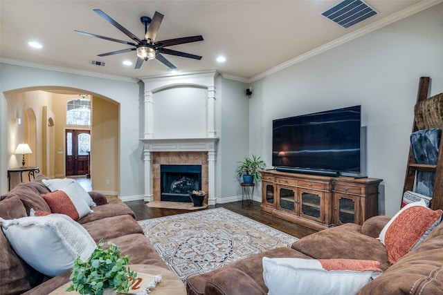 living room featuring a tiled fireplace, ornamental molding, dark wood-type flooring, and ceiling fan