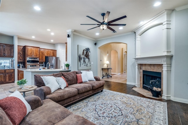 living room with ornamental molding, a tile fireplace, ceiling fan, and light wood-type flooring