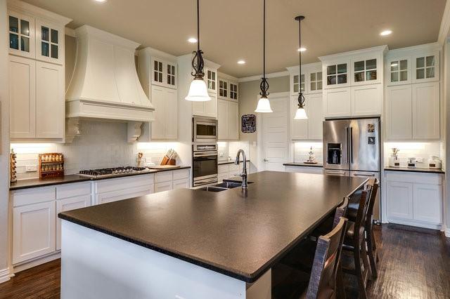 kitchen featuring decorative light fixtures, stainless steel appliances, custom range hood, and a center island with sink