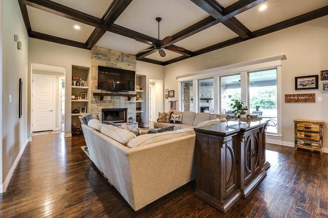 living room featuring dark wood-type flooring, ceiling fan, coffered ceiling, and a stone fireplace