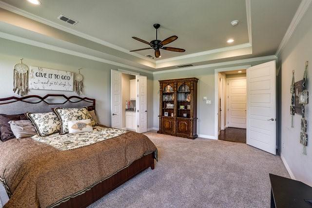 bedroom with ceiling fan, ornamental molding, a tray ceiling, and carpet floors