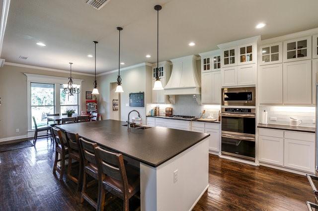 kitchen featuring sink, hanging light fixtures, stainless steel appliances, custom range hood, and a center island with sink