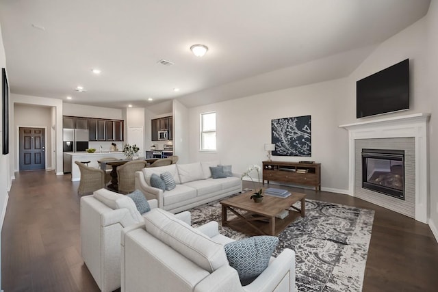 living room with a tiled fireplace, dark wood-type flooring, and vaulted ceiling