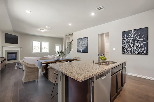 kitchen with a kitchen island with sink, dark hardwood / wood-style flooring, dark brown cabinets, and stainless steel dishwasher