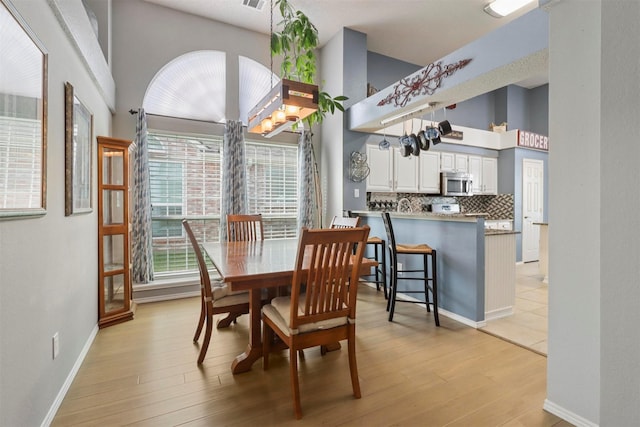 dining area featuring a towering ceiling, light wood-style floors, and baseboards