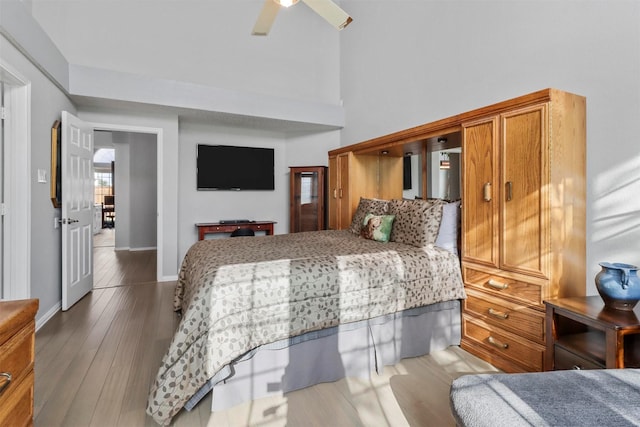 bedroom with a ceiling fan, a high ceiling, baseboards, and wood finished floors