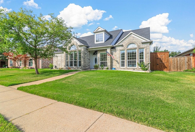 view of front of property featuring roof with shingles, fence, a front lawn, and brick siding