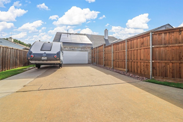 exterior space with driveway, a garage, fence, and roof mounted solar panels