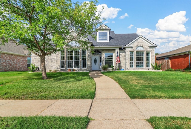 view of front of property featuring a shingled roof, a front yard, brick siding, and fence