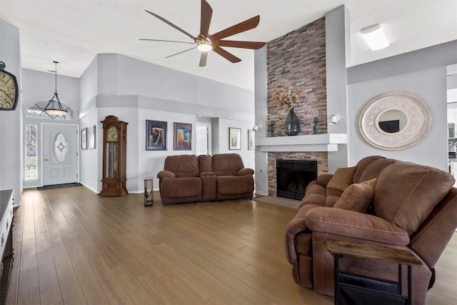 living room featuring a stone fireplace, a high ceiling, and wood finished floors