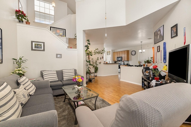 living room with an inviting chandelier, a towering ceiling, and light wood-type flooring