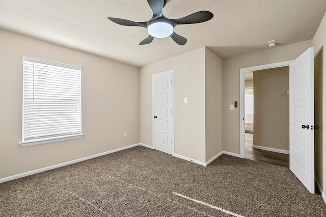 unfurnished bedroom featuring ceiling fan, dark carpet, and multiple windows