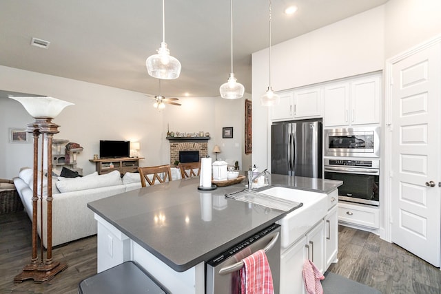 kitchen with a kitchen island with sink, stainless steel appliances, a fireplace, white cabinets, and decorative light fixtures