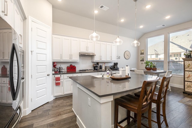 kitchen featuring appliances with stainless steel finishes, dark hardwood / wood-style floors, white cabinets, hanging light fixtures, and a kitchen island with sink