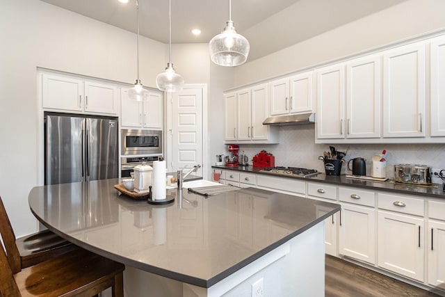 kitchen featuring white cabinetry, appliances with stainless steel finishes, decorative light fixtures, and a center island with sink