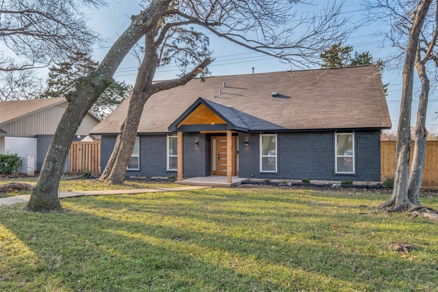 view of front of property featuring brick siding, a front lawn, a shingled roof, and fence