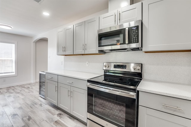 kitchen featuring gray cabinets, appliances with stainless steel finishes, backsplash, light hardwood / wood-style floors, and beverage cooler