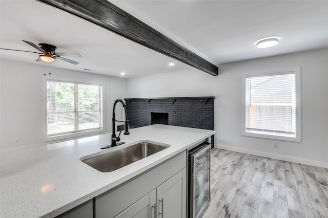 kitchen with sink, beam ceiling, wine cooler, light stone counters, and light wood-type flooring