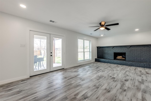 unfurnished living room with a fireplace, light hardwood / wood-style floors, french doors, and ceiling fan