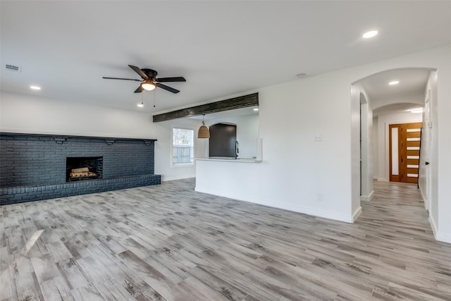 unfurnished living room with light wood-type flooring, visible vents, a fireplace, and arched walkways