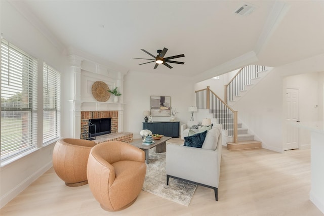 living room featuring visible vents, light wood-style flooring, stairway, crown molding, and a brick fireplace