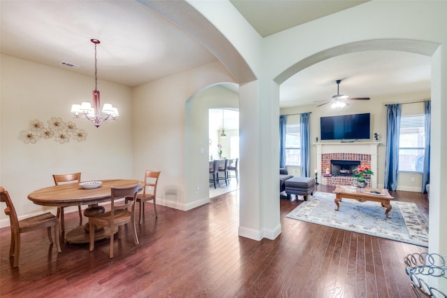 dining room with ceiling fan with notable chandelier, a fireplace, and dark hardwood / wood-style floors